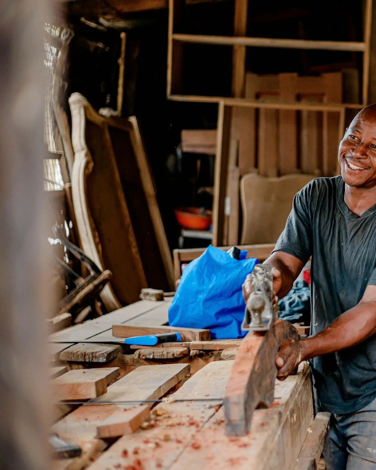 Un menuisier souriant qui rabote une planche dans son atelier.