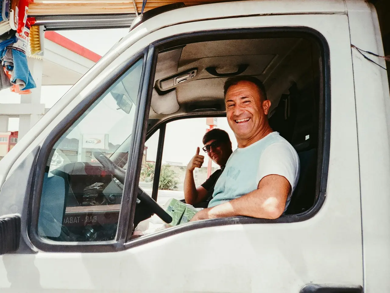 Un chauffeur souriant au volant de sa camionnette, vitre baissée.