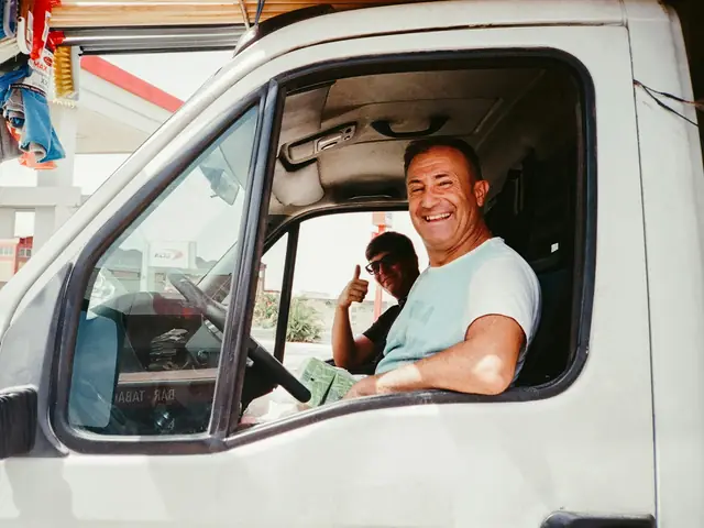 Un chauffeur souriant au volant de sa camionnette, vitre baissée.