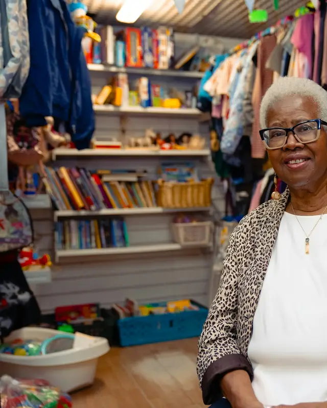 Une commerçante souriante dans sa boutique, devant ses rayonnages.